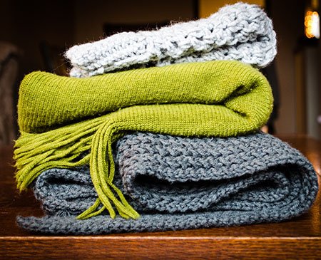 Several knitted scarves in different colours neatly stacked together